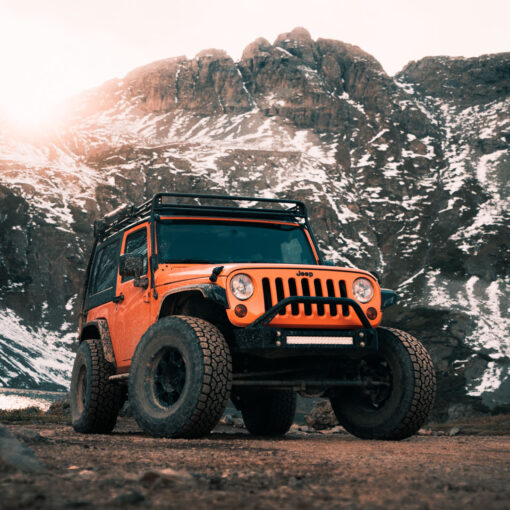 an orange jeep parked on a dirt road with mountains in the background