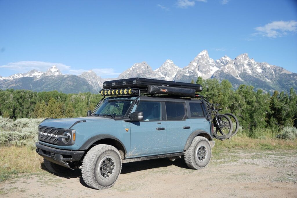 Turn Your Vehicle into a Gear Hauler: Roof Racks for Bikes, Kayaks & More | GOBI Racks Blue off-road SUV with rooftop gear and bikes mounted on the back, parked on a dirt path with snow-capped mountains in the background.