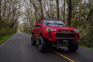 Lifted red Toyota 4Runner with a GOBI Racks roof rack on a forest road.
