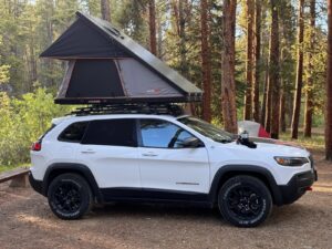 A white Jeep Cherokee KL with a tent attached to a GOBI Racks roof rack