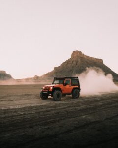 Orange Jeep with a GOBI Racks Roof Rack and Ladder Driving on Dirt Road